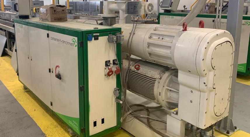 Extruder line with feed hopper, gearbox and drive motor alongside its control cabinet on a plant floor