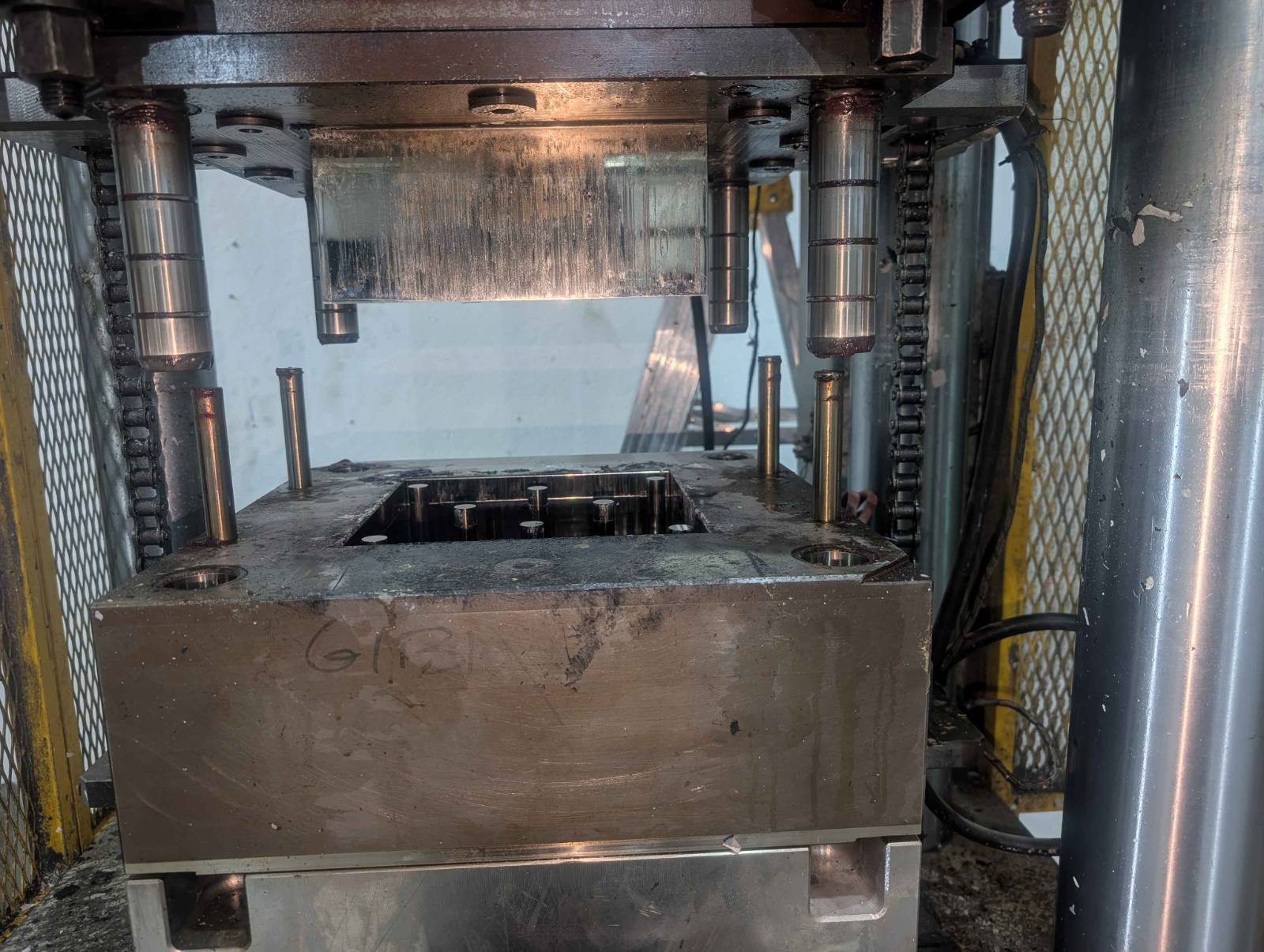 Hot press with the platens open, showing the heated upper platen, guide posts and lower die block