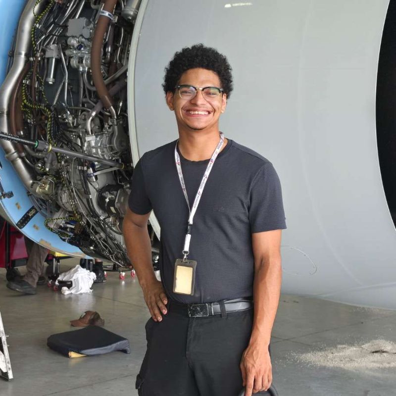 Lincoln Mendoza, founder of Mendoza Controls, in a hangar in front of an aircraft engine with the cowling open