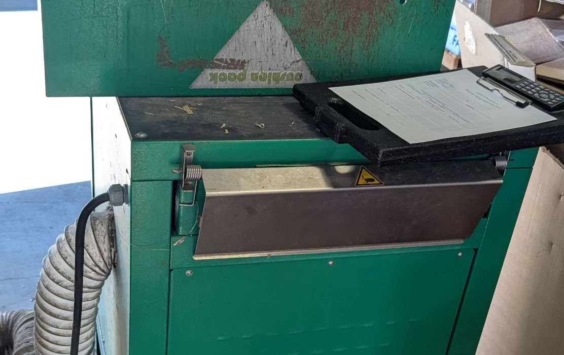 Shredder infeed throat with its spring-loaded guard flap and hazard label, control panel above and dust extraction ducting at the side